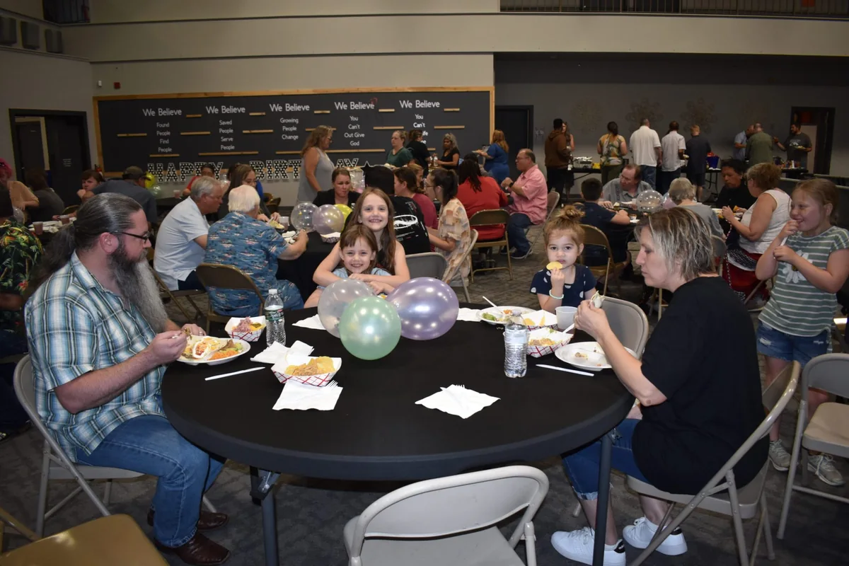 People of different ages sharing a meal around tables at God of No Limits, from the church’s July 2025 gallery.